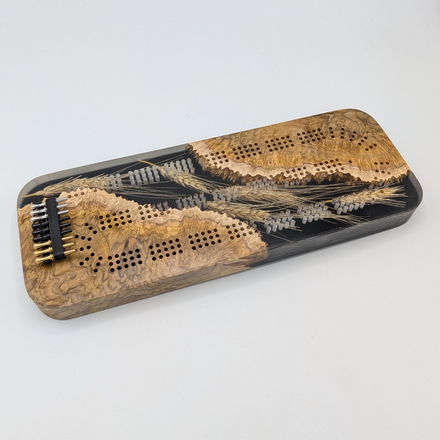 Wooden cribbage board with black pegs on a white surface
