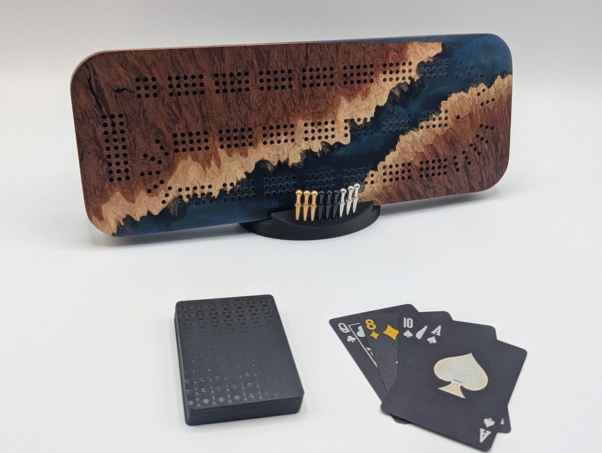 Origin Australian red mallee burl cribbage board with a diagonal channel of midnight blue epoxy, shown with pegs, cards and stand.
