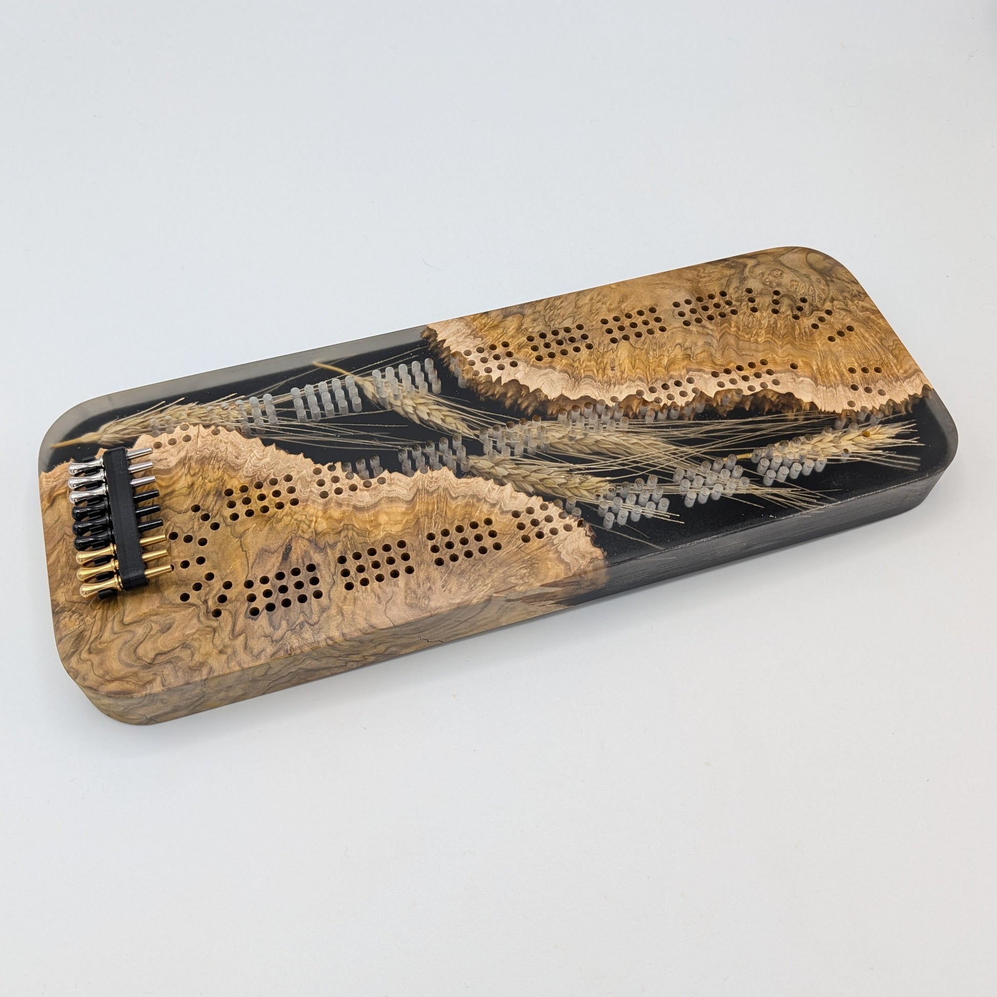 Wooden cribbage board with black pegs on a white surface