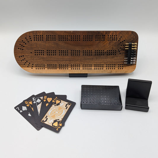 Wooden cribbage board with playing cards and black cases on a white surface