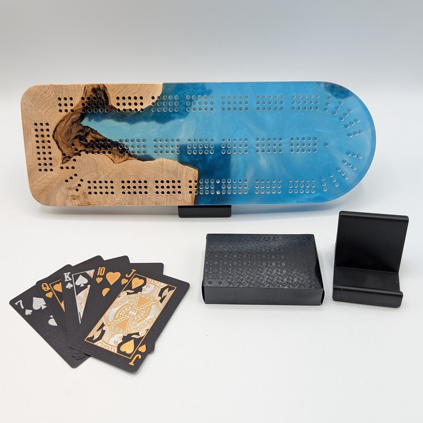 Cribbage board with blue and brown design, playing cards, and black stands on a white surface.