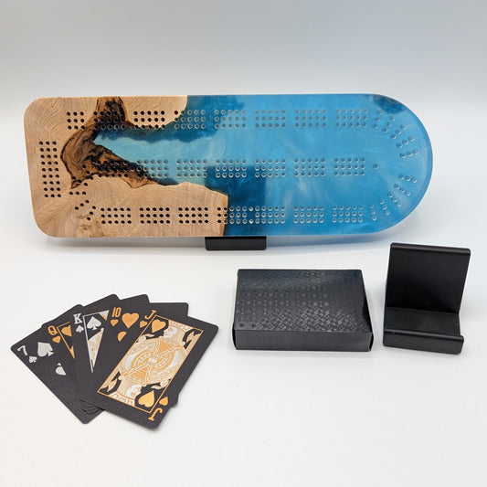 Cribbage board with blue and brown design, playing cards, and black stands on a white surface.