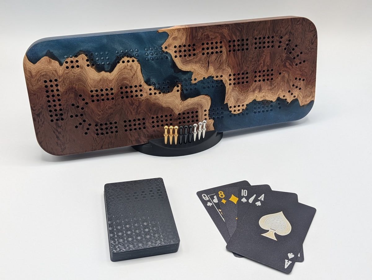 Origin cribbage board in Australian red mallee burl and midnight blue epoxy, shown on its stand with pegs and cards.