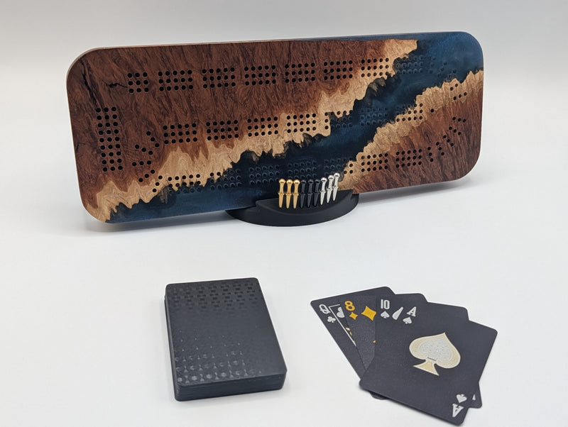 Origin Australian red mallee burl cribbage board with a diagonal channel of midnight blue epoxy, shown with pegs, cards and stand.